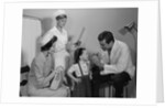 Mother sitting watching man pediatric doctor woman nurse checking on smiling little girl patient by Anonymous