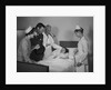 Man doctor woman nurse mother father seeing visiting smiling little girl patient in hospital bed by Anonymous