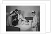 Man doctor woman nurse mother father seeing visiting smiling little girl patient in hospital bed by Anonymous