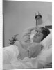 Ailing woman patient lying in hospital bed hand pressed to forehead by Anonymous