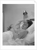 Ailing woman patient lying in hospital bed hand pressed to forehead by Anonymous