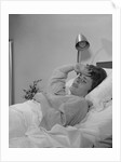 Ailing woman patient lying in hospital bed hand pressed to forehead by Anonymous