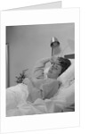 Ailing woman patient lying in hospital bed hand pressed to forehead by Anonymous