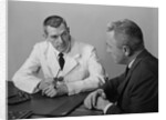 Doctor sitting at desk talking to male patient by Anonymous