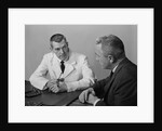 Doctor sitting at desk talking to male patient by Anonymous