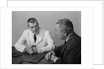 Doctor sitting at desk talking to male patient by Anonymous
