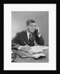 Businessman seated at desk talking on telephone smiling writing with pencil by Anonymous