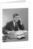 Businessman seated at desk talking on telephone smiling writing with pencil by Anonymous