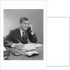 Businessman seated at desk talking on telephone smiling writing with pencil by Anonymous