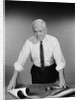 Middle aged man shirt sleeves rolled up standing blueprints on table by Anonymous