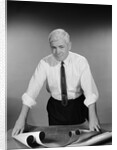 Middle aged man shirt sleeves rolled up standing blueprints on table by Anonymous