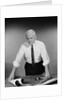 Middle aged man shirt sleeves rolled up standing blueprints on table by Anonymous