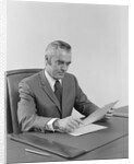 Businessman executive middle aged sitting at desk reading papers by Anonymous