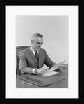 Businessman executive middle aged sitting at desk reading papers by Anonymous