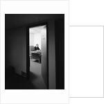 Executive businessman at desk seen working late through door ajar by Anonymous