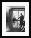Two men one seated shaking hands long wooden conference table by Anonymous