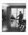 Two men one seated shaking hands long wooden conference table by Anonymous