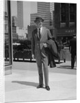 Businessman wearing suit hat carrying top coat standing on city street by Anonymous