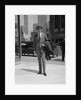Businessman wearing suit hat carrying top coat standing on city street by Anonymous