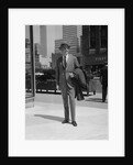 Businessman wearing suit hat carrying top coat standing on city street by Anonymous
