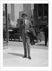 Businessman wearing suit hat carrying top coat standing on city street by Anonymous