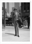Businessman wearing suit hat carrying top coat standing on city street by Anonymous