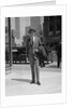 Businessman wearing suit hat carrying top coat standing on city street by Anonymous