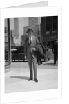 Businessman wearing suit hat carrying top coat standing on city street by Anonymous