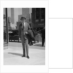 Businessman wearing suit hat carrying top coat standing on city street by Anonymous