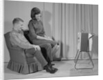 Couple man woman sitting chair watching portable television by Anonymous