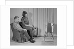 Couple man woman sitting chair watching portable television by Anonymous