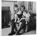 Man father sitting in chair with three children reading book by Anonymous