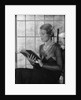 Elegant woman wearing pearls sitting by window reading book by Anonymous