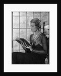 Elegant woman wearing pearls sitting by window reading book by Anonymous