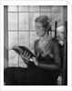 Elegant woman wearing pearls sitting by window reading book by Anonymous