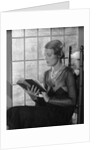 Elegant woman wearing pearls sitting by window reading book by Anonymous