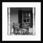Couple man woman sitting on porch in rocking chairs holding newspapers up hiding their faces by Anonymous