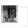 Couple man woman sitting on porch in rocking chairs holding newspapers up hiding their faces by Anonymous