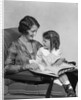 Mother & daughter smiling sitting in chair reading book by Anonymous