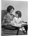 Mother & daughter smiling sitting in chair reading book by Anonymous