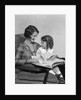 Mother & daughter smiling sitting in chair reading book by Anonymous