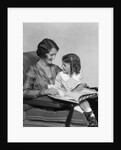 Mother & daughter smiling sitting in chair reading book by Anonymous