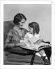 Mother & daughter smiling sitting in chair reading book by Anonymous
