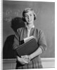 Teenage girl holding school books standing in front of blackboard by Anonymous