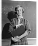 Teenage girl holding school books standing in front of blackboard by Anonymous