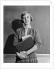 Teenage girl holding school books standing in front of blackboard by Anonymous