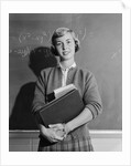 Teenage girl holding school books standing in front of blackboard by Anonymous
