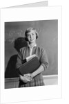 Teenage girl holding school books standing in front of blackboard by Anonymous