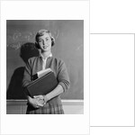 Teenage girl holding school books standing in front of blackboard by Anonymous