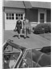 Couple carrying luggage walking towards convertible car in driveway by Anonymous